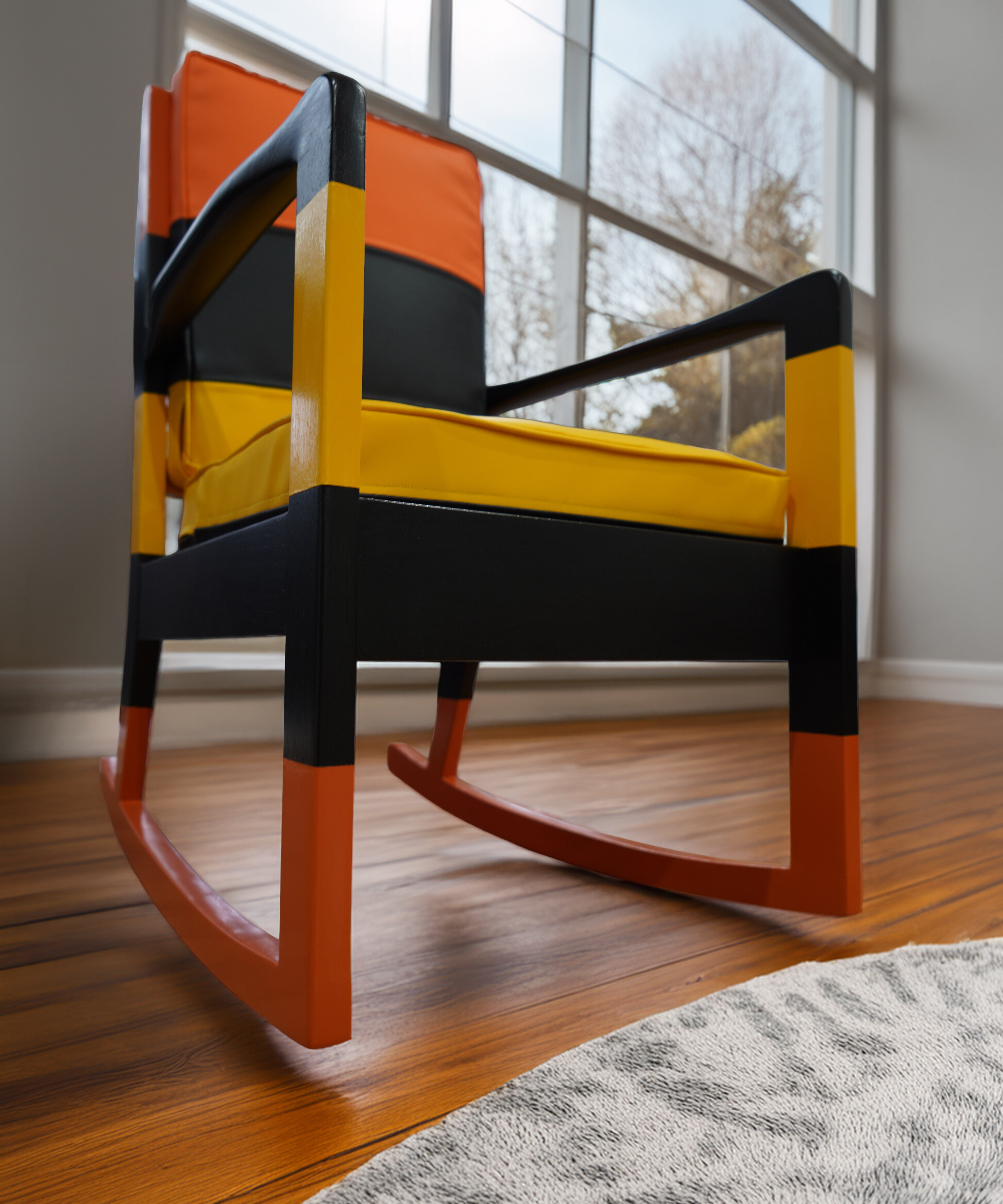 Orange, yellow, and black sculptural rocking chair photographed near a window.